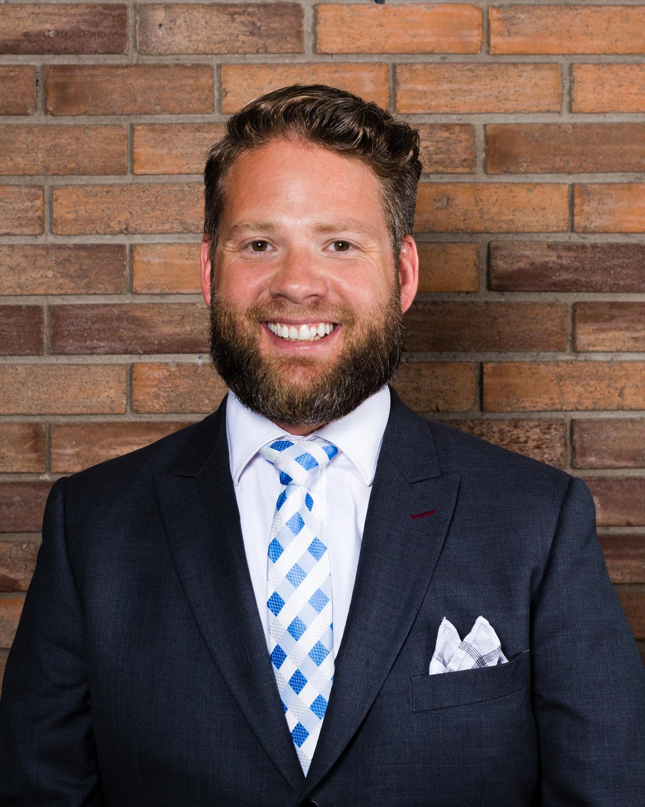 Norm smiling in a navy suit against a warm brick wall